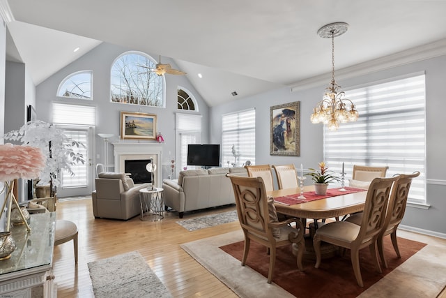 dining room featuring ceiling fan with notable chandelier, high vaulted ceiling, a fireplace, and light wood-style floors