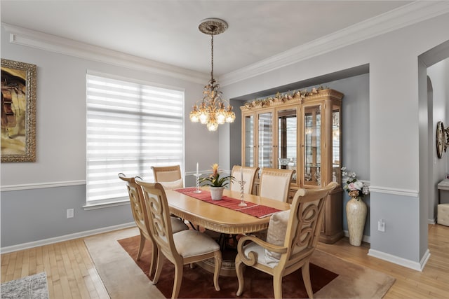 dining area with arched walkways, light wood finished floors, baseboards, and crown molding