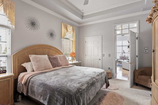 bedroom with ceiling fan, a raised ceiling, crown molding, and light colored carpet