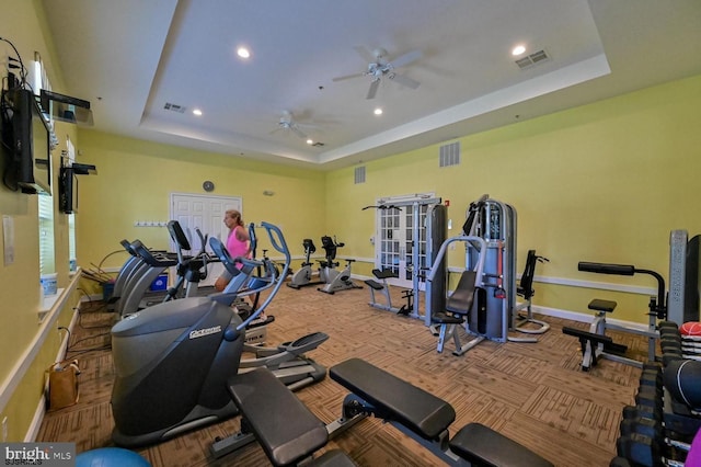 workout area with a ceiling fan, a tray ceiling, and visible vents