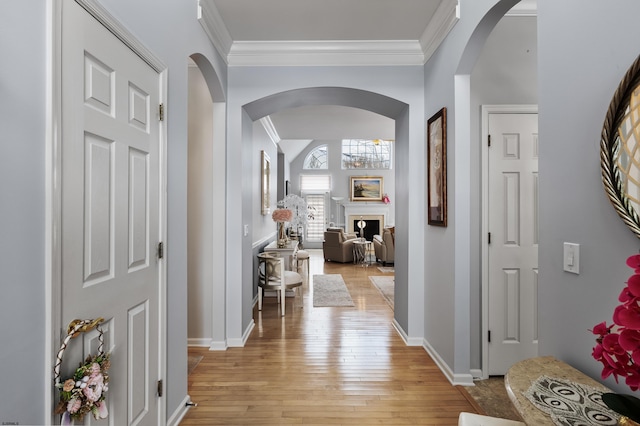 foyer entrance with light wood-style flooring, a fireplace, ornamental molding, and arched walkways