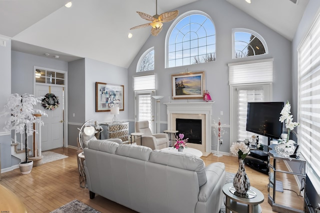 living room with ceiling fan, high vaulted ceiling, a premium fireplace, baseboards, and light wood finished floors