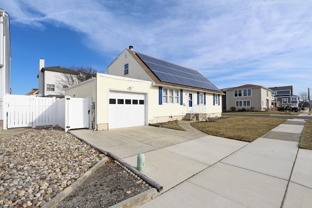 view of front of home featuring an attached garage, solar panels, fence, driveway, and a residential view