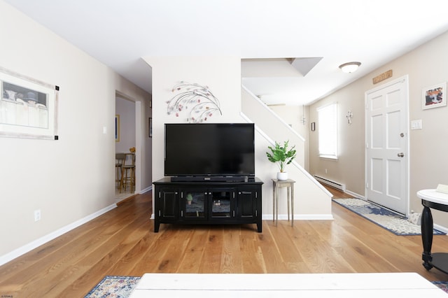 living area featuring a baseboard radiator, light wood-style flooring, baseboards, and stairs