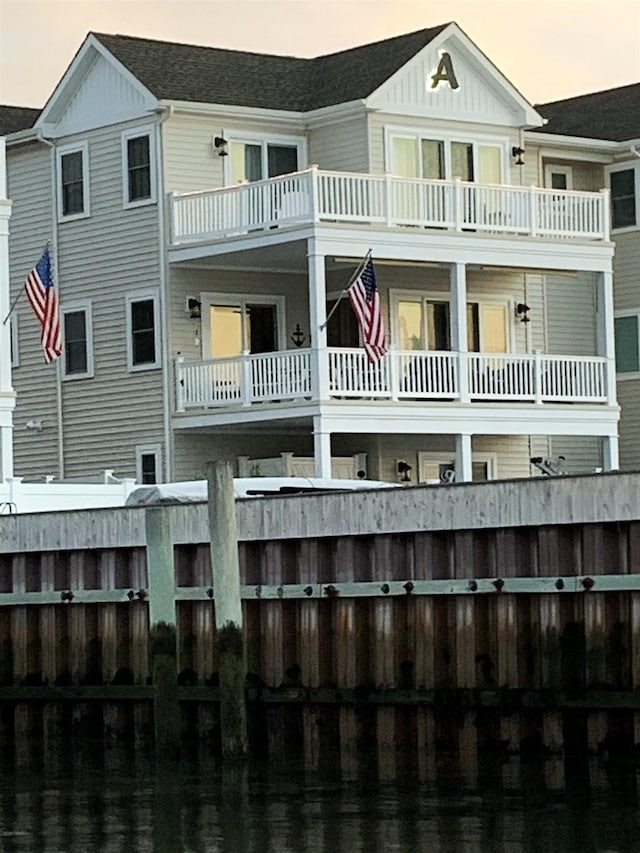 back of house at dusk featuring a balcony and board and batten siding