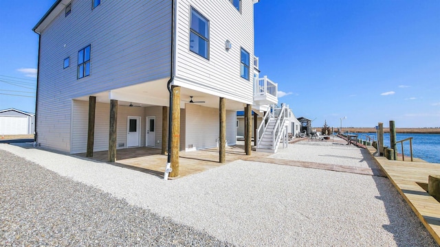 back of property with ceiling fan, a patio, a water view, stairway, and a carport