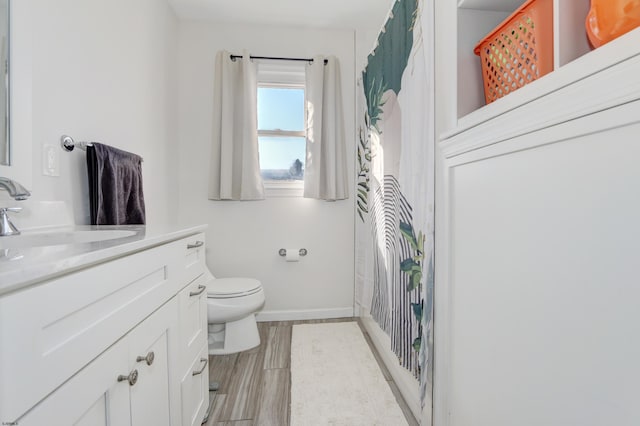 bathroom with toilet, baseboards, wood finished floors, and vanity