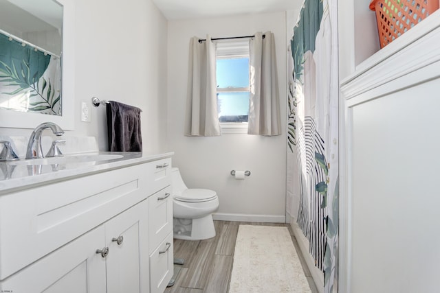 bathroom featuring baseboards, vanity, toilet, and wood finished floors