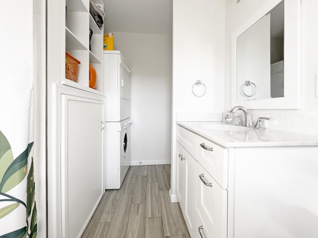 clothes washing area with laundry area, baseboards, stacked washer / drying machine, light wood-type flooring, and a sink