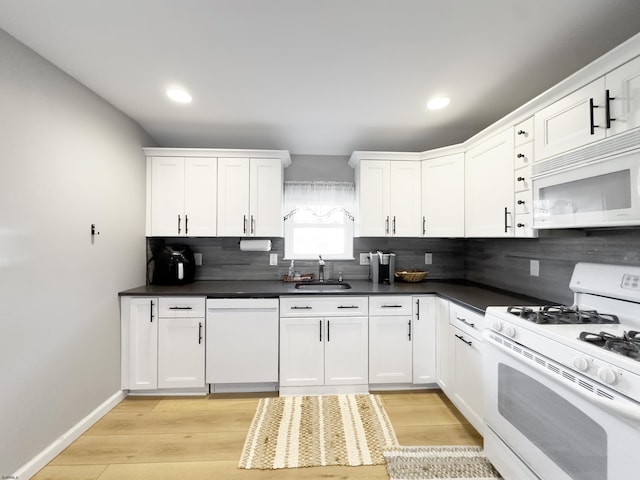 kitchen with dark countertops, backsplash, white cabinetry, a sink, and white appliances