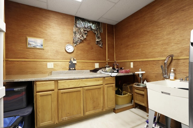 kitchen featuring a paneled ceiling, light countertops, wood walls, and a sink