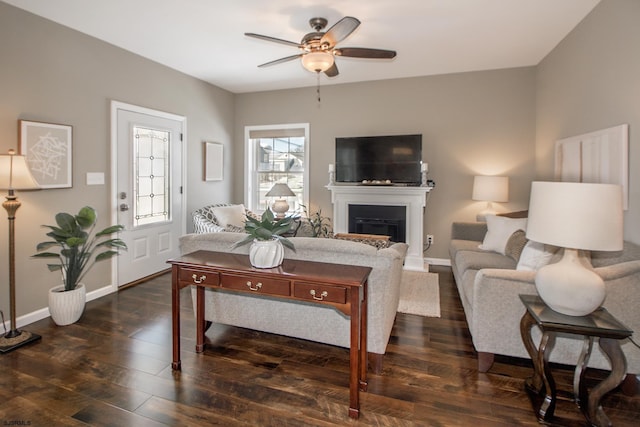 living area with a fireplace, baseboards, dark wood finished floors, and a ceiling fan