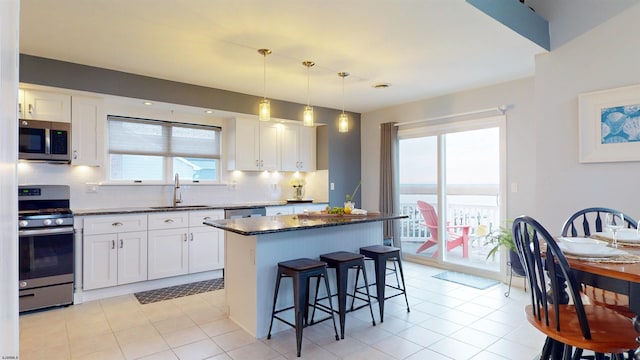 kitchen with stainless steel appliances, a sink, white cabinetry, a center island, and pendant lighting