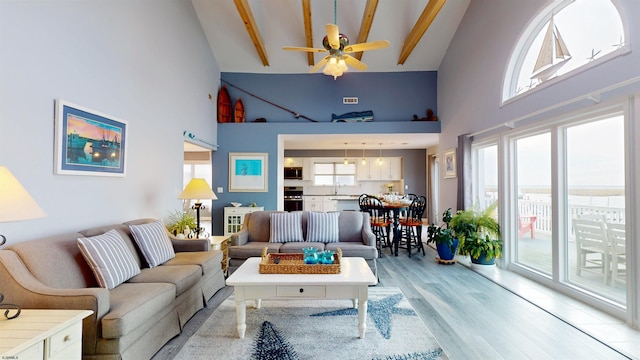 living room with ceiling fan, high vaulted ceiling, light wood-type flooring, and beam ceiling