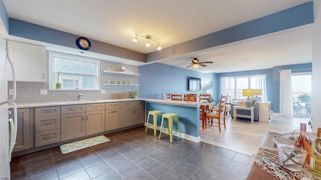 kitchen featuring gray cabinetry, a peninsula, a sink, light countertops, and decorative backsplash