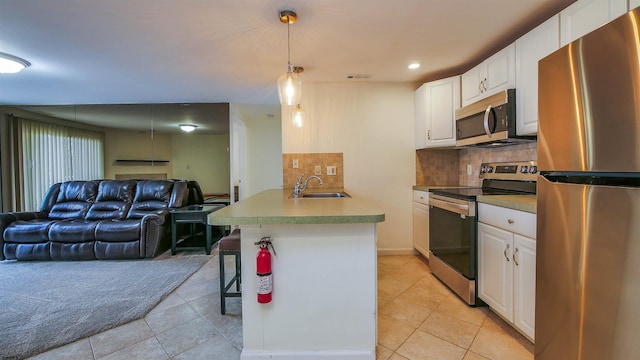 kitchen featuring white cabinets, open floor plan, stainless steel appliances, a kitchen bar, and pendant lighting