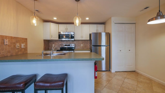 kitchen featuring white cabinets, appliances with stainless steel finishes, a kitchen breakfast bar, a peninsula, and a sink