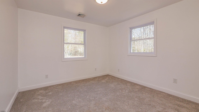 empty room featuring plenty of natural light, visible vents, and light colored carpet