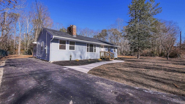 ranch-style house with a chimney and aphalt driveway