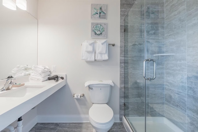 bathroom with a stall shower, baseboards, a sink, and toilet