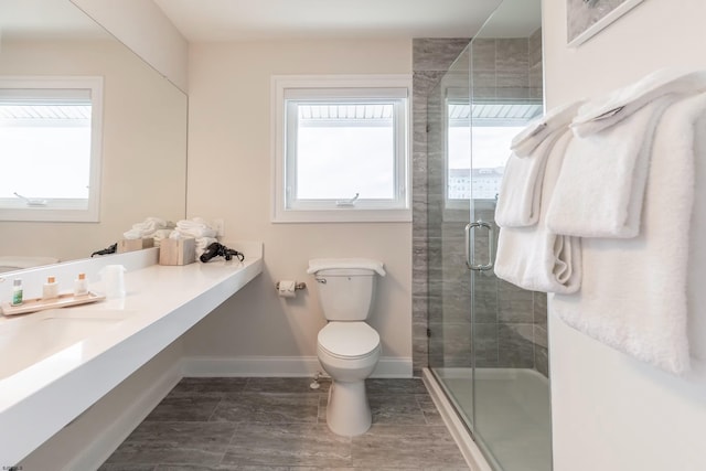 bathroom with a stall shower, toilet, plenty of natural light, and baseboards