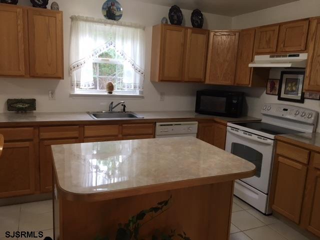 kitchen with under cabinet range hood, white appliances, a kitchen island, a sink, and light countertops