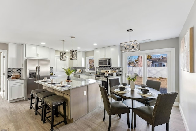 kitchen featuring stainless steel appliances, white cabinets, a kitchen island, and hanging light fixtures