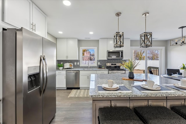 kitchen featuring a kitchen breakfast bar, white cabinets, appliances with stainless steel finishes, decorative backsplash, and pendant lighting