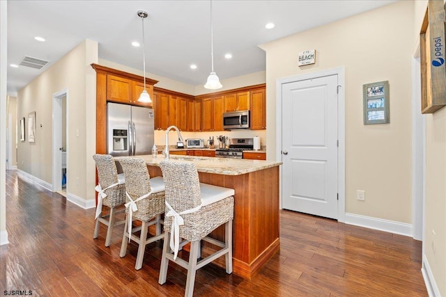 kitchen with stainless steel appliances, a kitchen breakfast bar, hanging light fixtures, light stone countertops, and a center island with sink