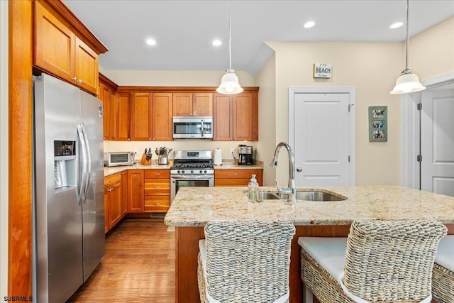 kitchen featuring a center island with sink, appliances with stainless steel finishes, light stone counters, decorative light fixtures, and a sink