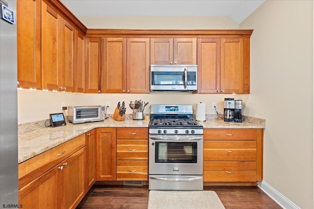 kitchen featuring dark wood-style floors, stainless steel appliances, brown cabinets, and a toaster