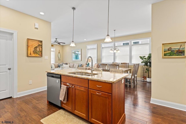 kitchen with pendant lighting, a center island with sink, stainless steel dishwasher, a sink, and light stone countertops