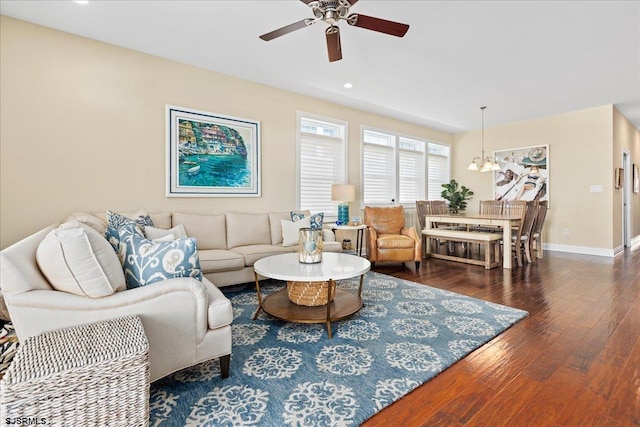 living area with dark wood-type flooring, recessed lighting, baseboards, and ceiling fan with notable chandelier