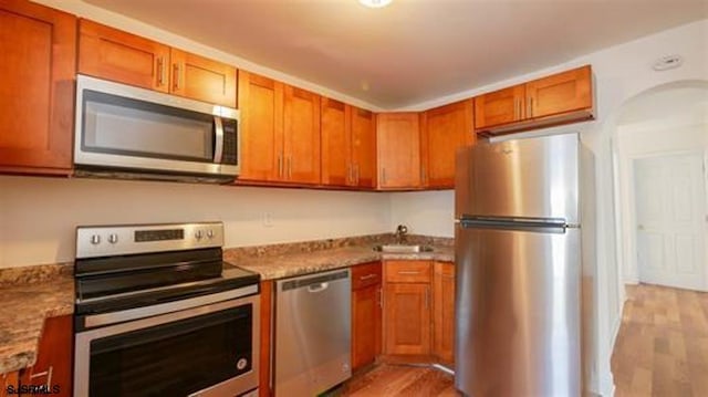 kitchen with stainless steel appliances, light wood-style floors, a sink, and light stone countertops