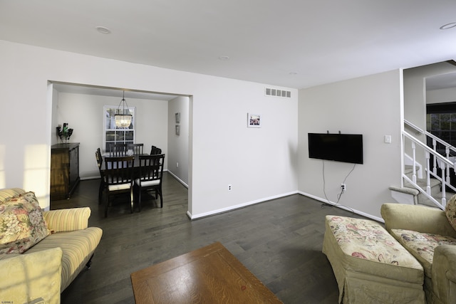 living room featuring dark wood-style flooring, visible vents, baseboards, stairway, and an inviting chandelier