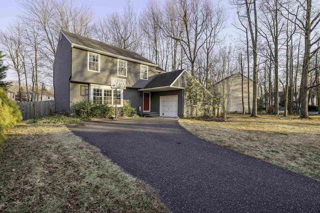 colonial home with driveway, an attached garage, and fence