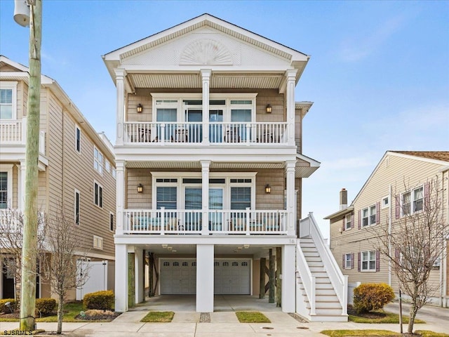 coastal home featuring a porch, an attached garage, a balcony, concrete driveway, and stairway