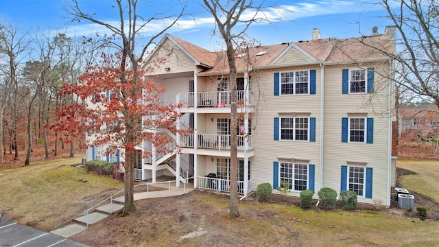 view of front of house with a balcony, central air condition unit, stairway, a chimney, and a front yard