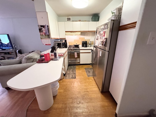 kitchen with a peninsula, appliances with stainless steel finishes, light wood-type flooring, and light countertops