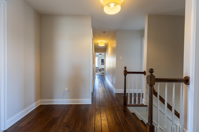 hall featuring dark wood-style floors, an upstairs landing, and baseboards