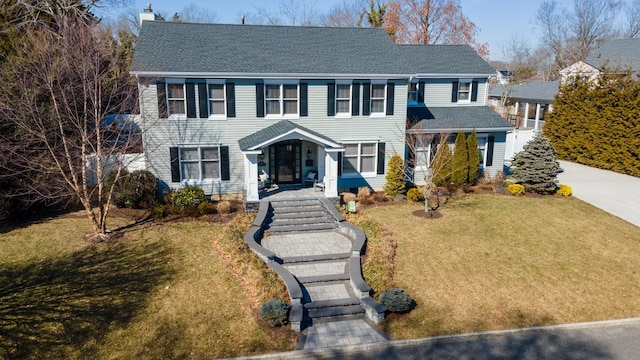 colonial home with roof with shingles, a chimney, and a front lawn