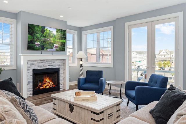 living area with light wood-style floors, baseboards, a wealth of natural light, and a stone fireplace