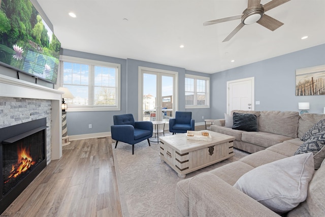 living room with french doors, a stone fireplace, plenty of natural light, and light wood-style floors