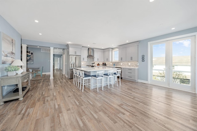 kitchen featuring a breakfast bar, light countertops, decorative backsplash, high quality fridge, and wall chimney exhaust hood