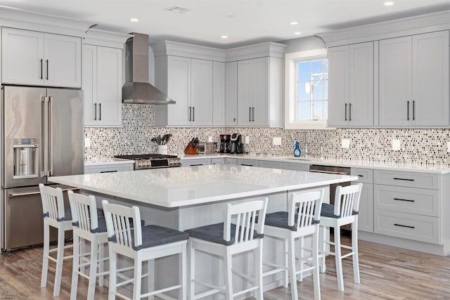 kitchen featuring range, light wood-style flooring, a kitchen island, wall chimney range hood, and high end fridge