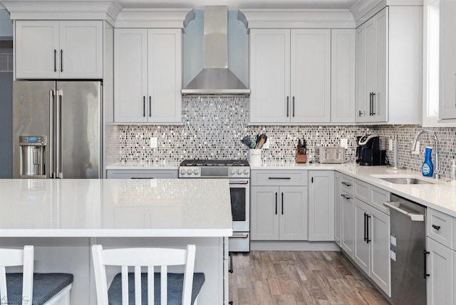 kitchen featuring stainless steel appliances, light countertops, decorative backsplash, a sink, and wall chimney range hood