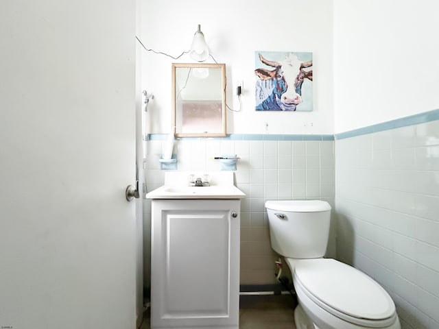 bathroom featuring a wainscoted wall, vanity, toilet, and tile walls