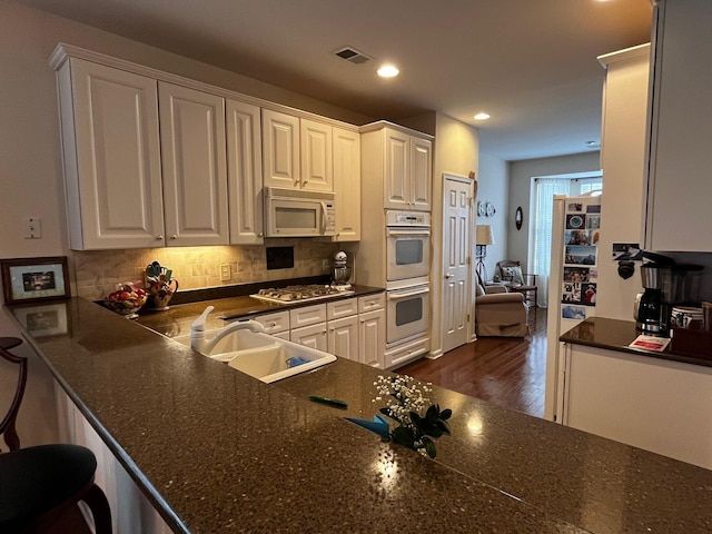 kitchen with dark wood-style flooring, tasteful backsplash, appliances with stainless steel finishes, white cabinets, and a sink