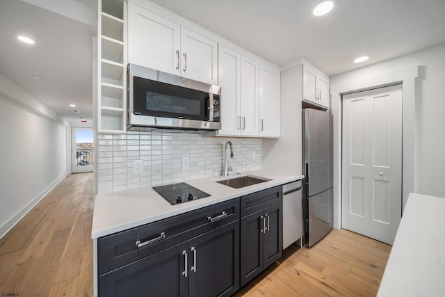kitchen featuring light wood-style flooring, stainless steel appliances, a sink, white cabinets, and tasteful backsplash