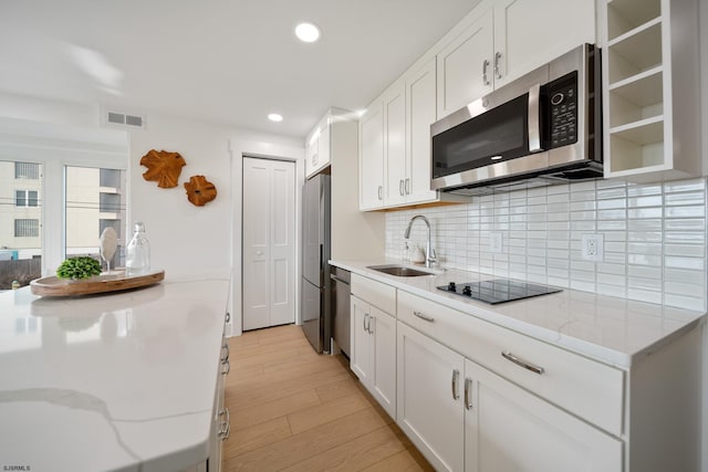kitchen featuring tasteful backsplash, visible vents, stainless steel appliances, light wood-type flooring, and a sink